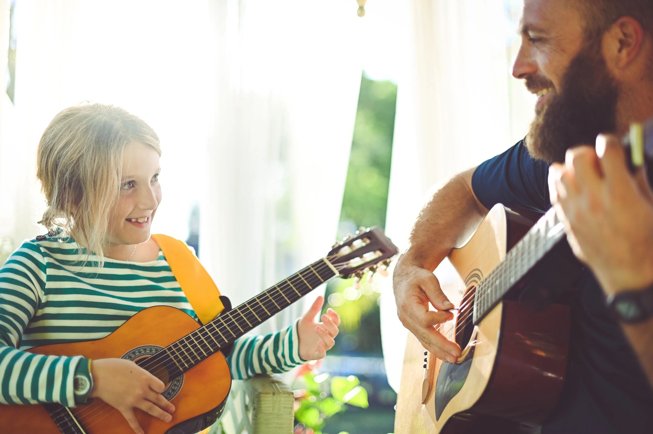 Adult and child playing guitar together outdoors